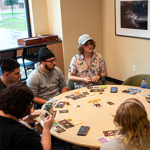 A group of students play a card game together at a round table in a Living Learning Community.