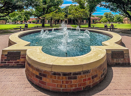 A fisheye view of the fountain, with a student working at a picnic table in the background, in the MSU Texas quad.