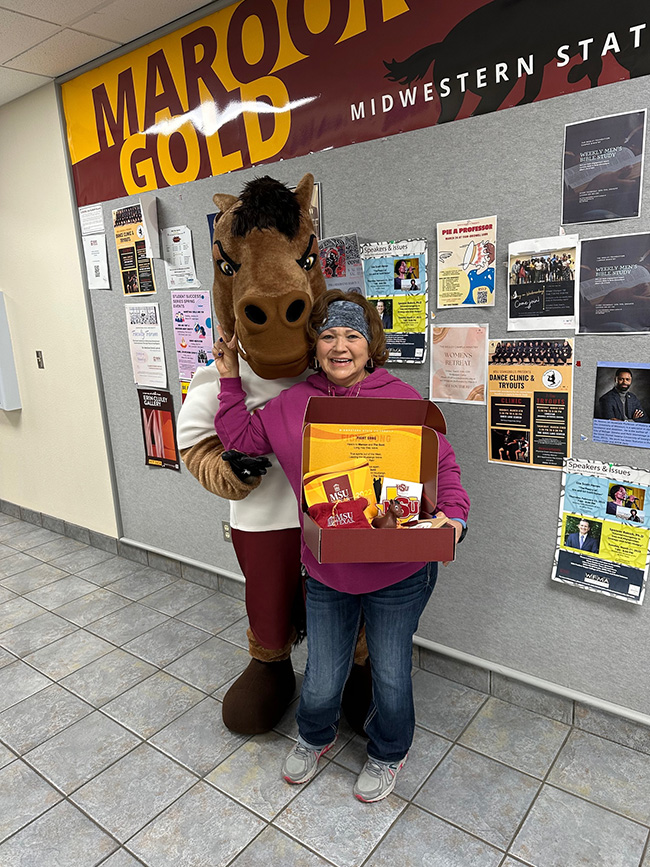 Maverick the Mustang posting with an employee holding the MSU Texas spirit box she won inside the Clark Student Center on March 10, 2023.