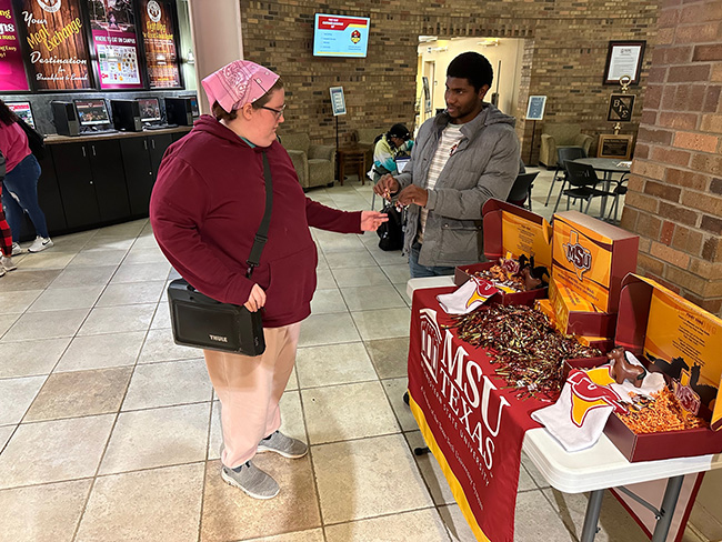 Student accepting a Maroon March button in the lobby of the Dillard College of Business Administration, March 8, 2023.