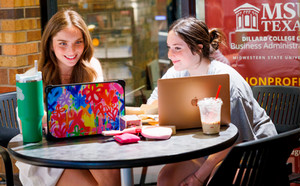 Two students with laptops smiling