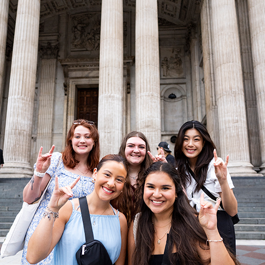 A group of five students smile and hold up the Mustangs Hand Sign during study abroad in London.