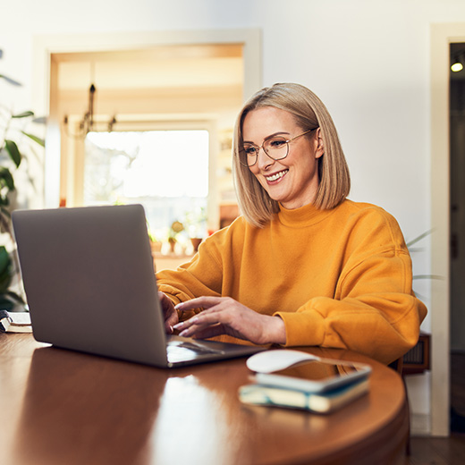 A woman happily works on her laptop at home.