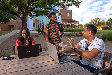 A group of international students work together on their laptops outside of Centennial Hall.