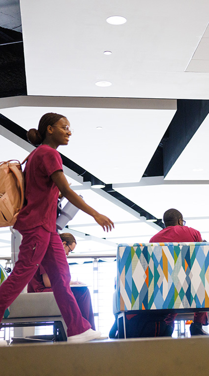 A group of Health Sciences and Human Services students gather and converse in Centennial Hall, while one smiling student walks past.