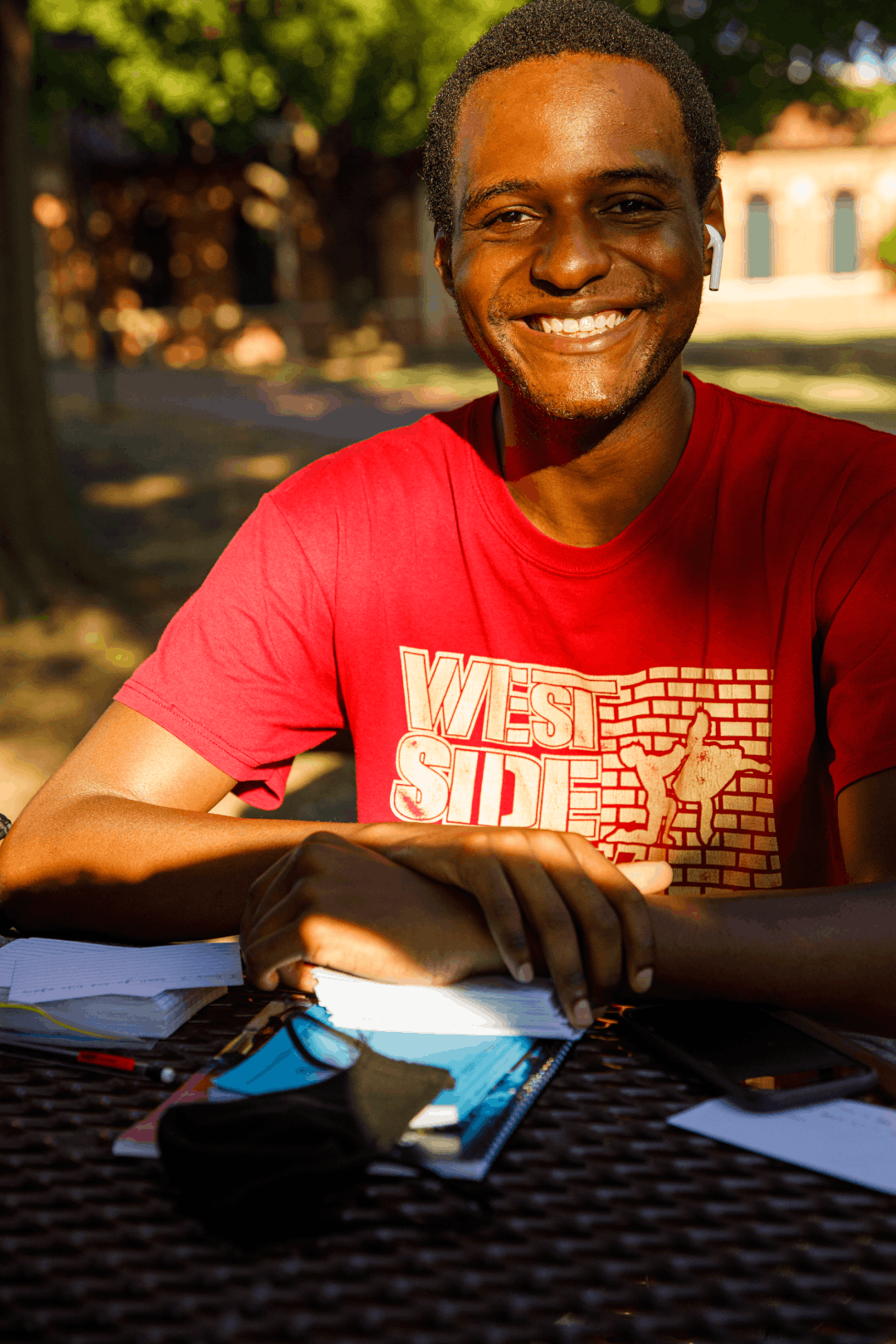 Student sitting outside at a picnic table smiling at the camera.