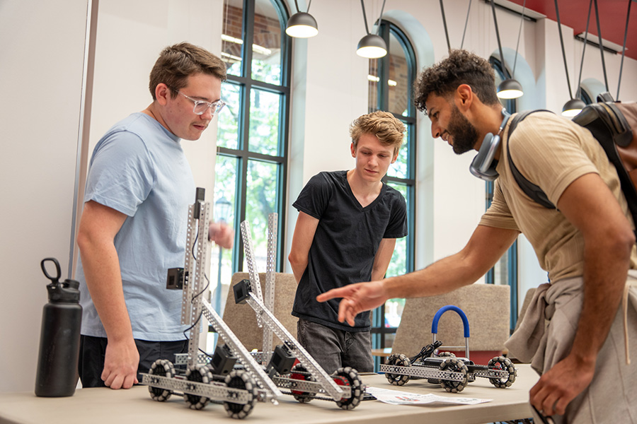 Two students converse with a third student over their engineering project inside the McCoy College of Science, Mathematics & Engineering lobby in Bolin Hall.
