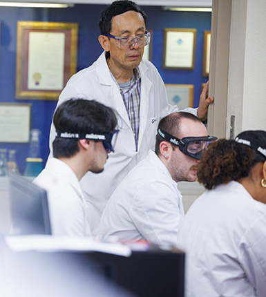 Three students work together as the professor oversees their work in Bolin.