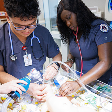Two Respiratory students work together with an infant mannequin in Centennial Hall.