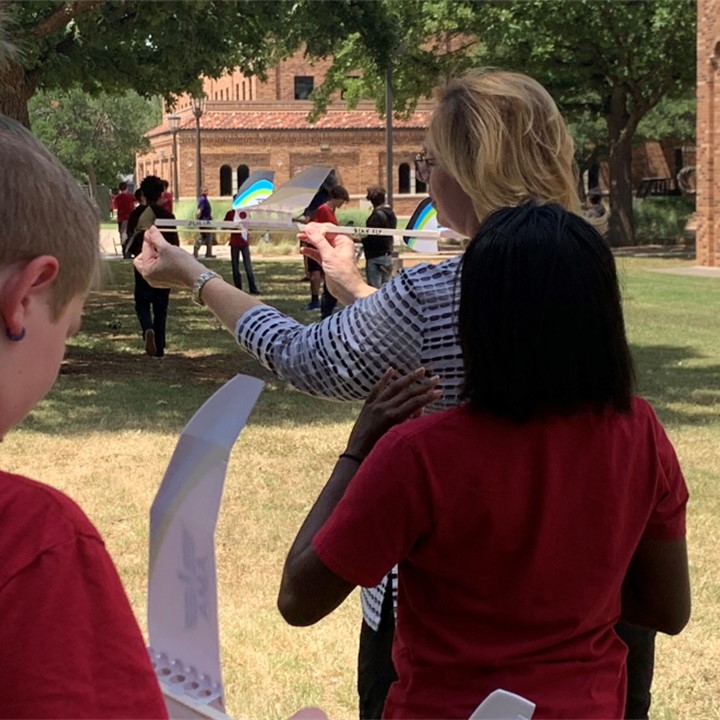 Students outside with their plane projects on the quad during YES Camp 2022. One student is receiving help for her project plane.