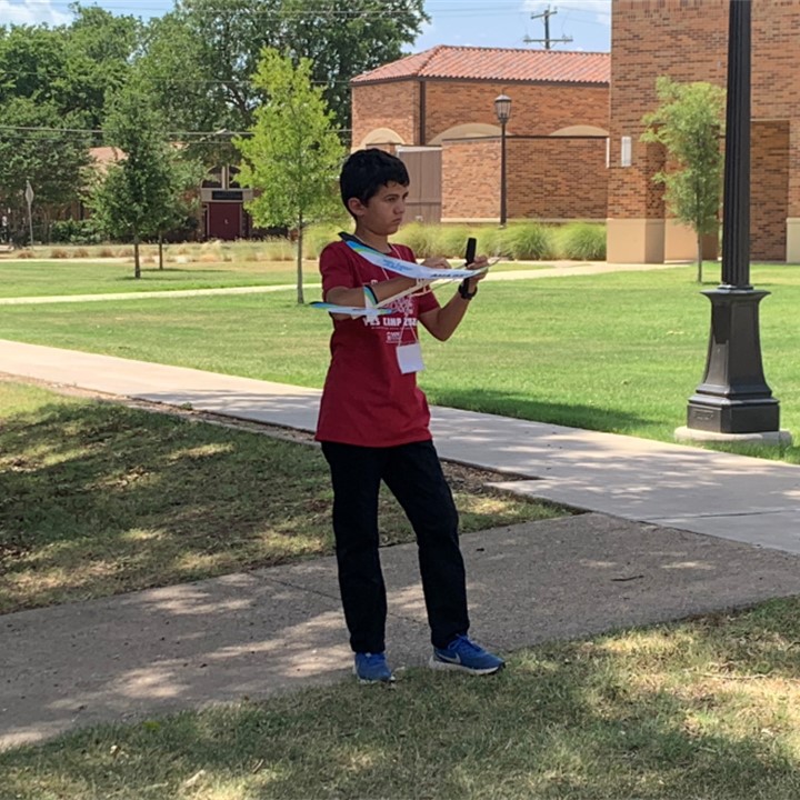 One student is outside on the quad, holding his project plane from YES Camp 2022.