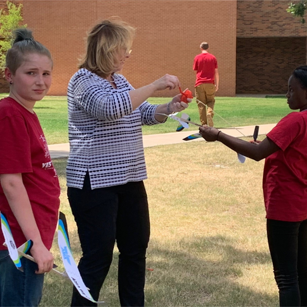 Two students get some instruction and feedback regarding their project planes, while outside, during YES Camp 2022.
