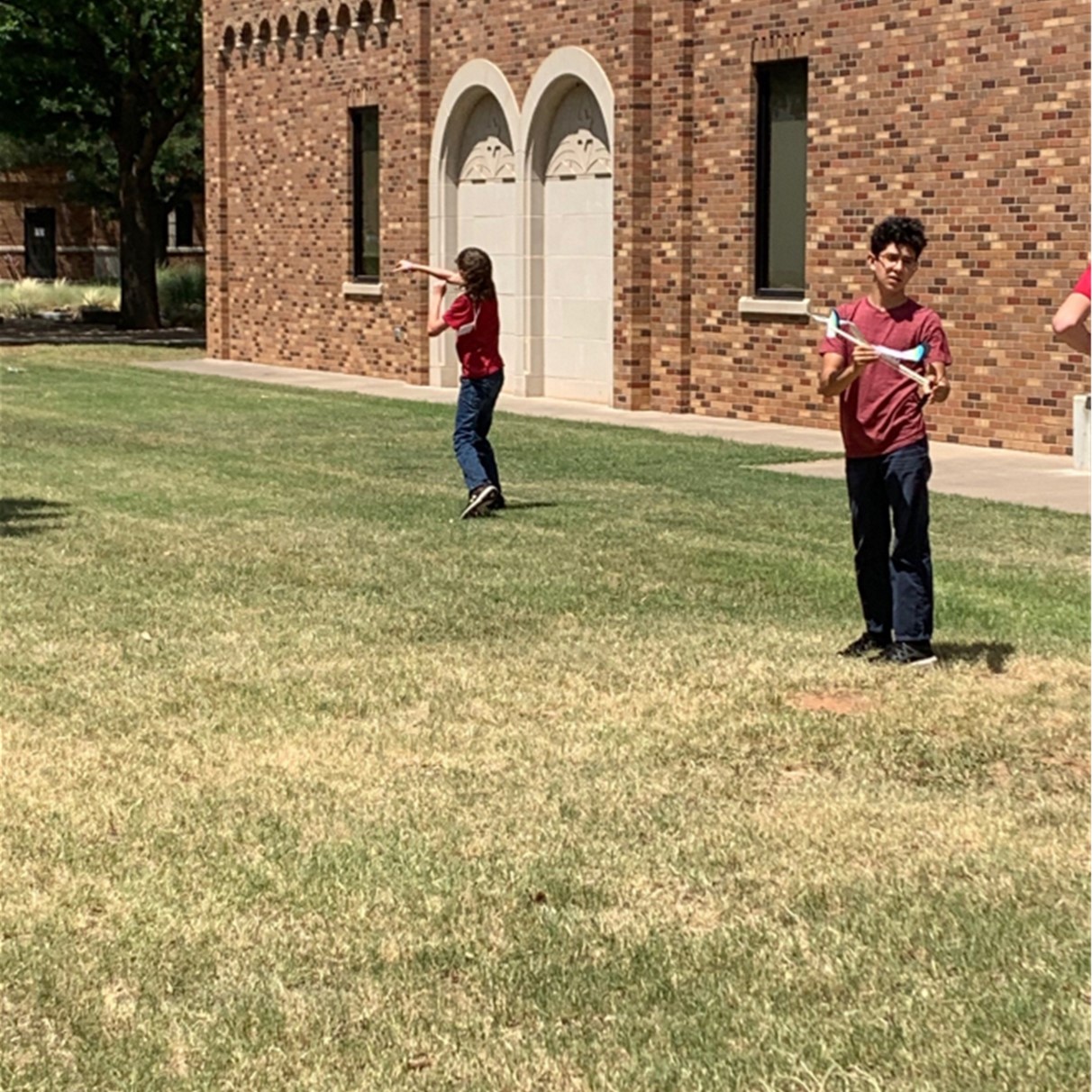 Three students work with their project planes outside on the quad during YES Camp 2022.