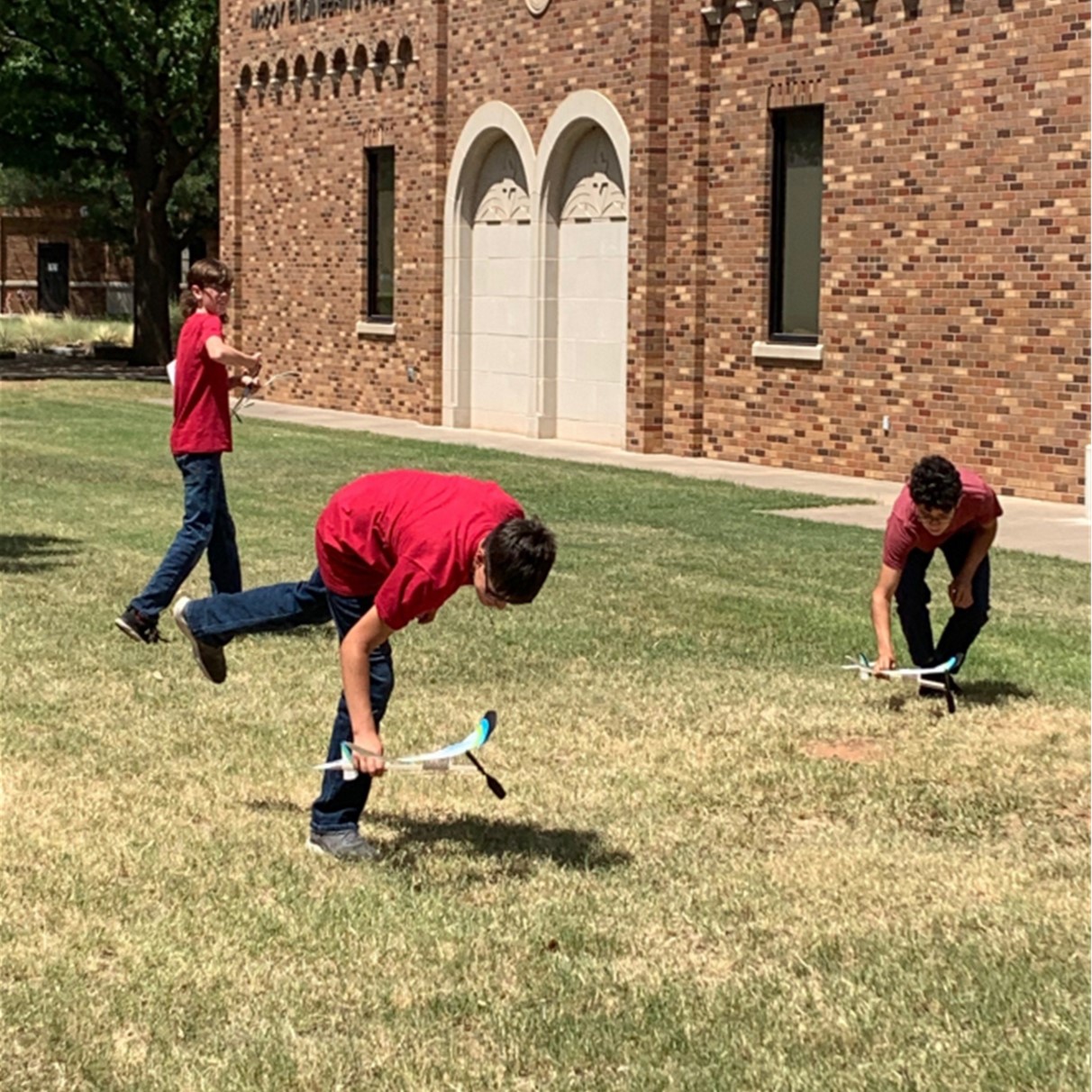 Three students working and playing with their project planes outside on the quad during YES Camp 2022.