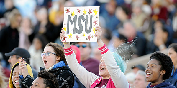 Student at a football game holding a side that says MSU.