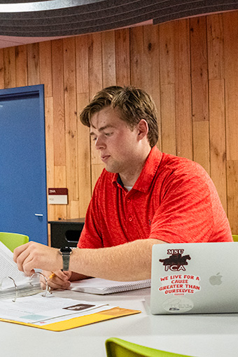 A student works on his laptop and inside a binder of papers inside Moffett Library.