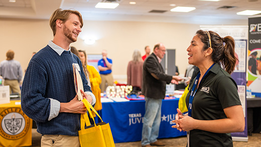 A student and potential employer converse in the foreground while others converse in the background at the Career Fair hosted by the Career Management Center.