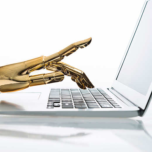 Gold plated robotic hand rests its hand to type on a laptop computer to represent artificial intelligence operating as a human being.