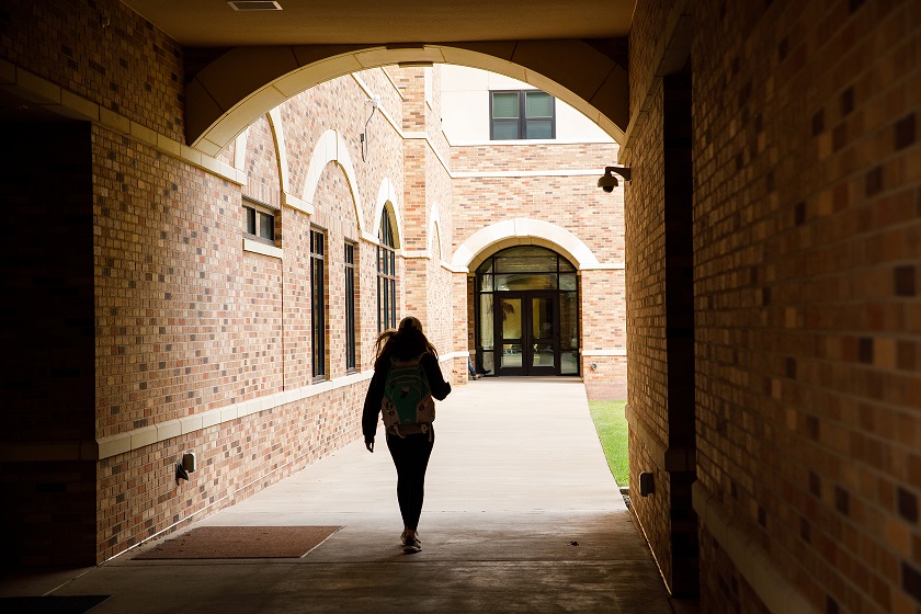 Student walking to a university building underneath an outdoor archway.
