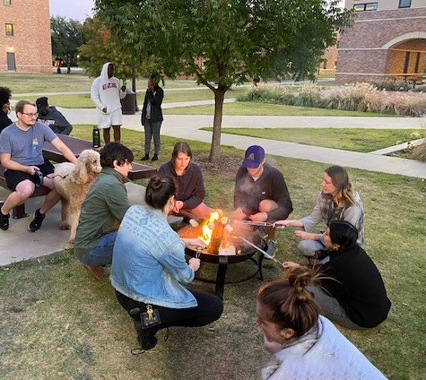 A group of students gathered around a bonfire roasting marshmallows in the Legacy Courtyard.