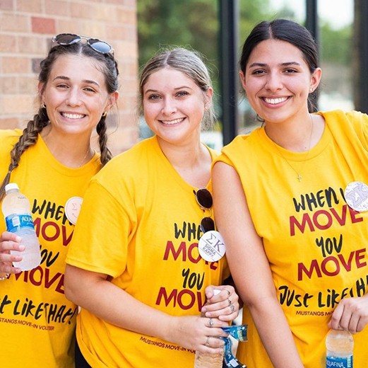 Three smiling students pose together outside of Legacy Hall during Move In Day.