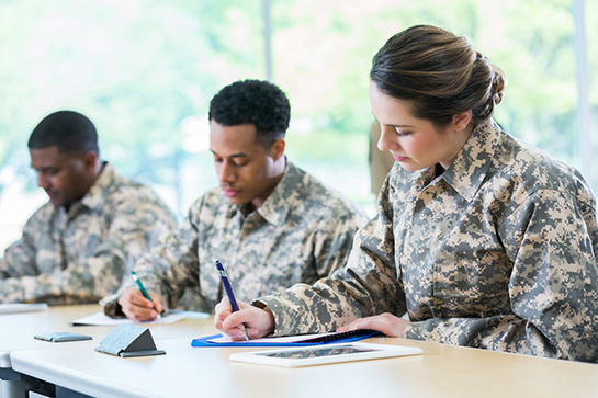 Three Military students take notes at their desk.