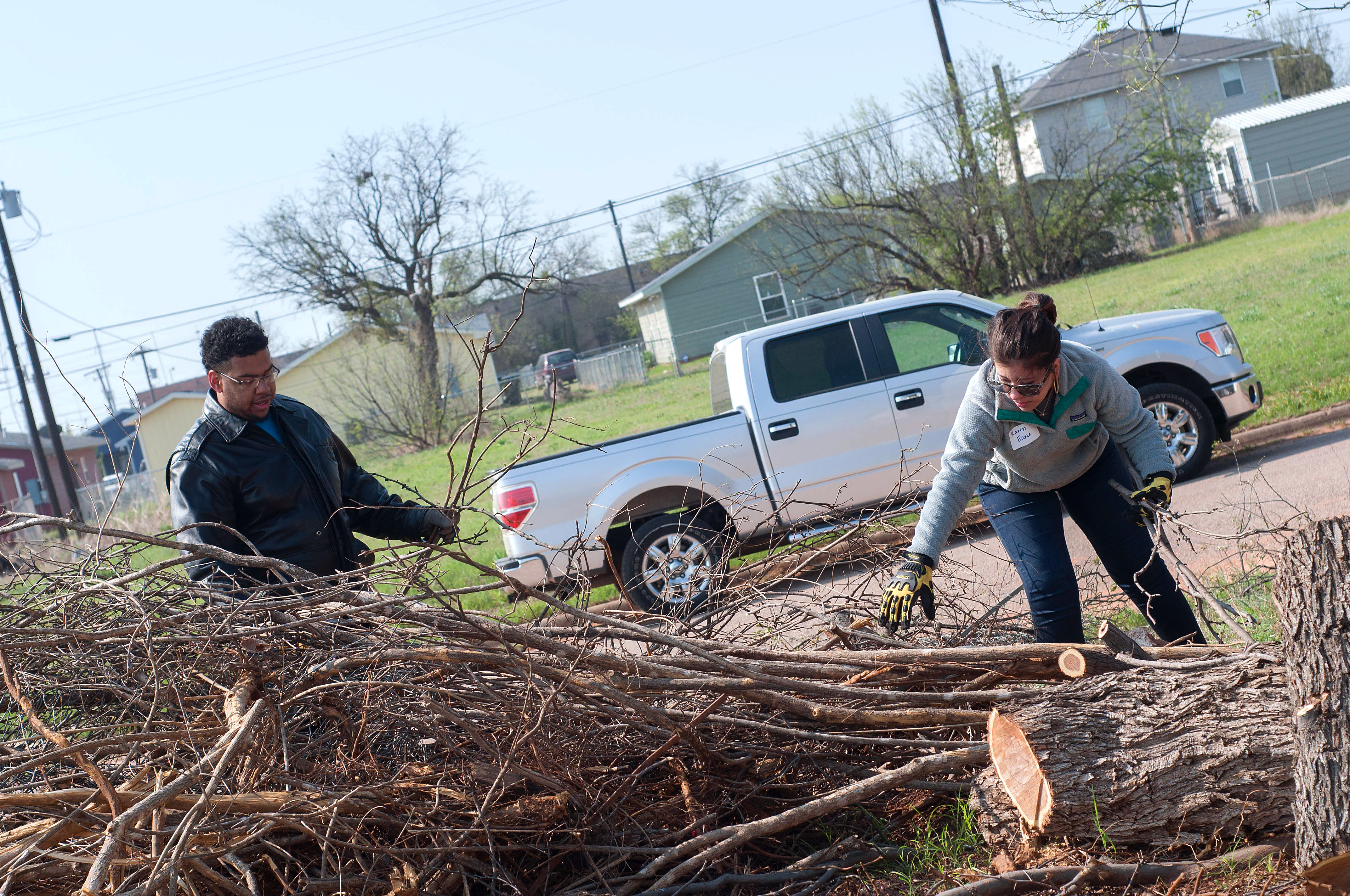 Two students cleaning up a Habitat for Humanity lot after a tree was cut down, pulling at branches and logs