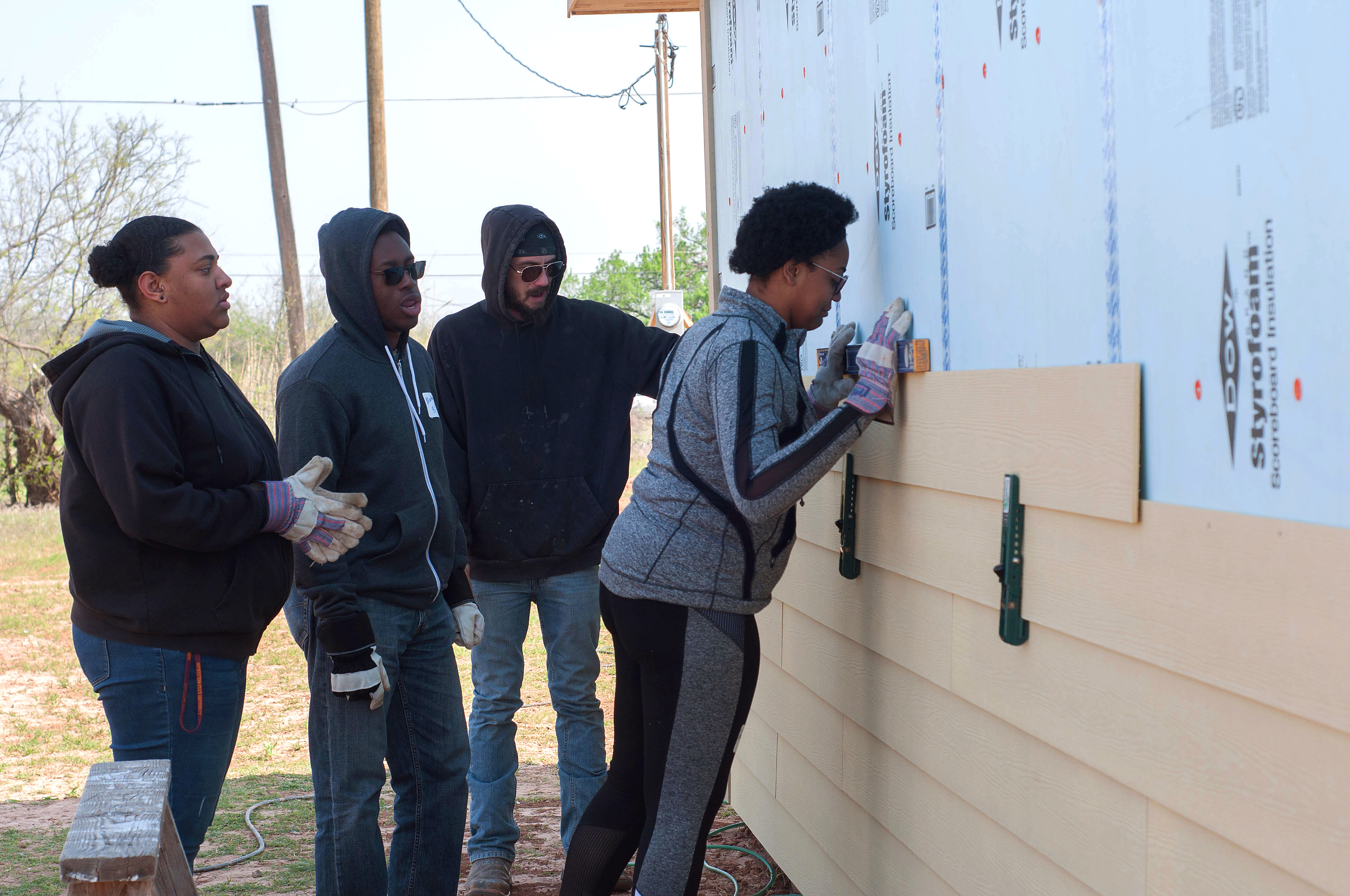 Four students working together to put up exterior paneling on a Habitat for Humanity home. 