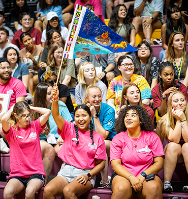 A group of students smile and wave a flag during an event inside D. L. Ligon Coliseum.