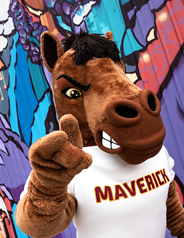 Maverick T. Mustang, the MSU Texas Mascot, holding up the Mustangs Hand Sign posing against a brightly painted mural in downtown Wichita Falls, Texas.