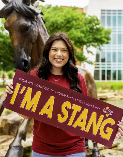 Student in front of a horse Sculpture holding a sign