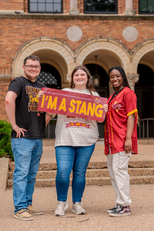 Three students holding a stang sign