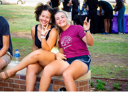 Two smiling students hold up the Mustangs Hand sign.