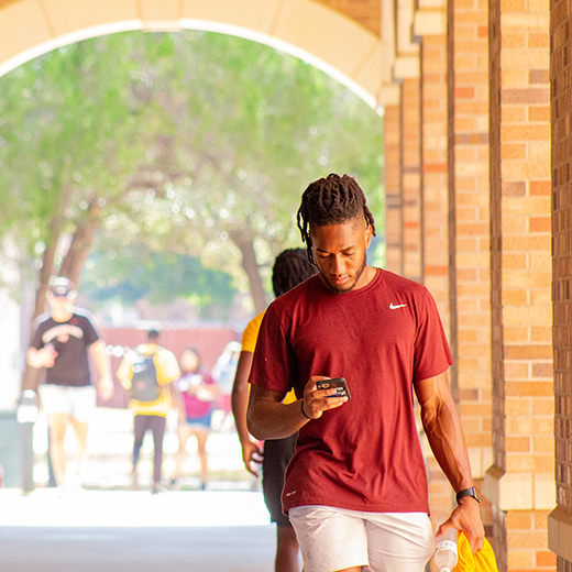 A student looks at his phone while walking, as other students are behind him, near Legacy Hall.