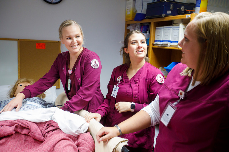 Three nursing students next to a hospital bed.