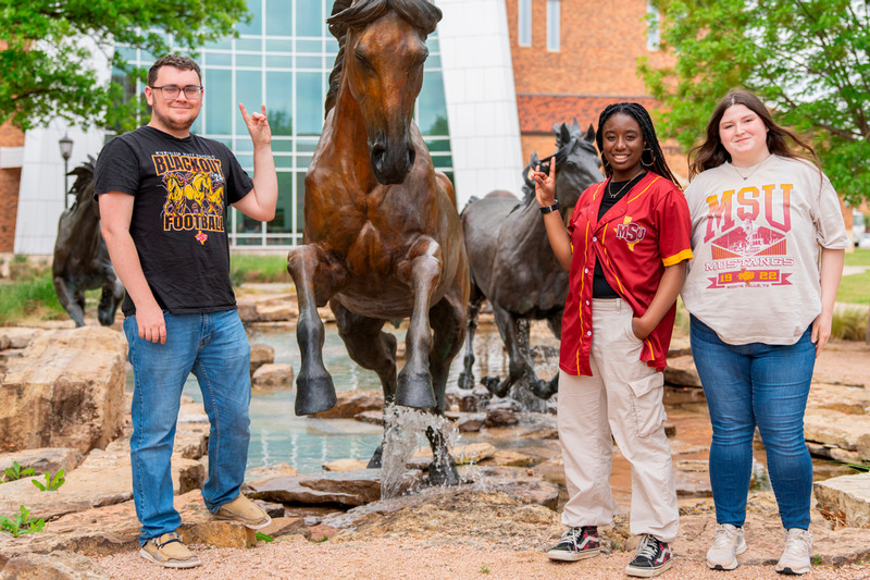 Three students standing in front of a mustang statue.